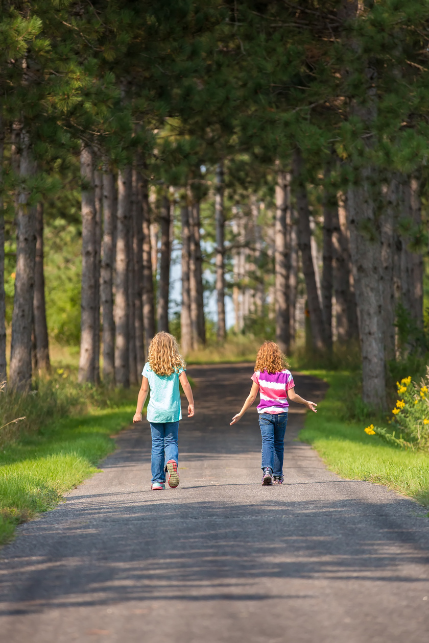 Two Girls Walking on Paved Park Trail Through Woods